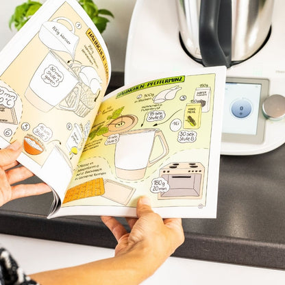 Das aufgeschlagene Rezeptbuch mit dem Thermomix® im Hintergrund